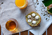 Leckerer Toast mit Avocado und Mozzarellakugeln, dekoriert mit Leinsamen und Sonnenblumenkernen und serviert auf einer Serviette neben Gläsern mit frischem Orangensaft und Kräutertee