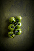 Overhead view of bunch of whole tomatoes with pedicels on green background with painted waves