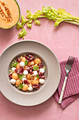 From above exotic melon, mozzarella and prosciutto salad on pink colorful background