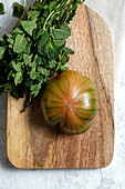 From above of fresh striped green and red tomato placed on wooden cutting board with bunch of mint stems