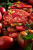 High angle of sliced tomato with salt placed on wooden chopping board among ripe red tomatoes with water drops