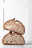 Halves of tasty sourdough bread with brown crust placed on table against white backdrop