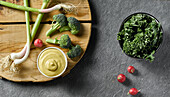 Top view of fresh lettuce on bowl near onion broccoli and radish placed on wooden cutting board with mustard