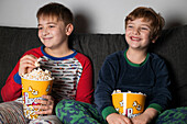 Young little brothers sitting comfortable on sofa with popcorn bucket while eating and watching TV