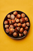 Top view of fresh unpeeled hazelnuts placed in bowl on yellow background