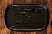 Top view of black fork and knife placed near sealed canned food on rectangular black tray
