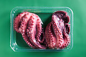 Roher rosa Oktopus in Plastikbox auf grünem Hintergrund