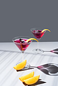 Composition of glass filled with red fruit cocktail near orange slides and zest placed on concrete table against grey background