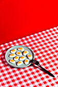 From above of plate with jelly eggs and fork placed on red checkered napkin against scarlet background