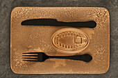 Top view of black fork and knife placed near sealed canned food on rectangular copper tray