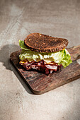 High angle of appetizing sandwich with fresh crusty bread above lettuce leaves and bacon on wooden board