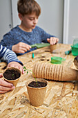Crop anonymous children at table with green seedling growing in carton cup with soil in house
