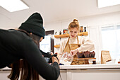 Crop anonymous photographer with photo camera against blogger with jar of icing sugar and muffins in baking cups at home