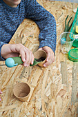 From above of crop anonymous kid with gardening shovel filling eco cup with earth at table