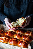Female baker opening puff freshly baked hot cross buns on baking tray