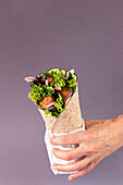 Cropped unrecognizable person hands holding vegan falafel wrap on colorful purple background