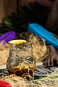 Tiki-Glasbecher mit Schnaps auf dem Rand eines Holztisches in einem Raum mit trockenem Gras auf unscharfem Hintergrund