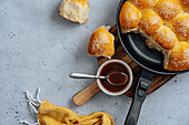 From above of tasty pull apart bread rolls with sesame seeds in frying pan served on wooden cutting board with sweet sauce