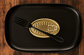 Top view of black fork placed near sealed canned food on rectangular black tray