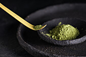 Spoon with dried matcha tea leaves on black tableware for traditional oriental ceremony