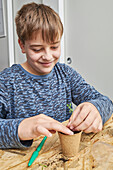 Content child planting green seedling in cardboard cup with earth at table in house in daytime