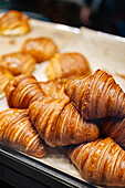 Haufen leckerer, knuspriger, brauner Croissants auf Pergament in einer Vitrine für moderne leichte Konditoreiwaren mit Gebäck auf unscharfem Hintergrund
