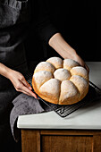 High angle of crop unrecognizable baker standing at counter with fresh bread buns placed on baking pan in kitchen