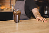 Crop anonymous male barista serving glass of freshly brewed aromatic coffee with ice cubes on counter