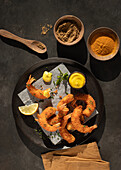 From above still life with plate of lemon and mustard battered prawns with two bowls of turmeric and curry spices