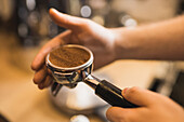 High angle of crop anonymous male barista preparing ground coffee in portafilter for making espresso in cafe