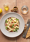 From above dish of pasta with arugula, salami and walnuts on a table surrounded by oil, lemon and cutlery