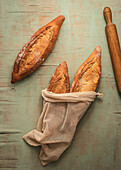 Top view composition of delicious crispy artisan sourdough bread loaves packed in burlap bags on green background