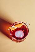 Glass of bitter alcoholic Negroni cocktail served with ice and orange peel on light surface