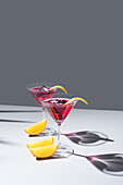 Composition of glass filled with red fruit cocktail near orange slides and zest placed on concrete table against grey background