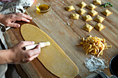 Unrecognizable person preparing raviolis and pasta at home. She is painting the pasta with eggs
