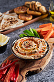 From above of delicious hummus and slices of assorted vegetables served near bottle of oil and bowl of lemon pieces on gray marble table