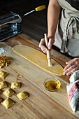Unrecognizable person preparing raviolis and pasta at home. She is painting the pasta with eggs