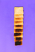 Top view of row of sliced bread ranging from fresh and soft to burnt and cracked against violet background