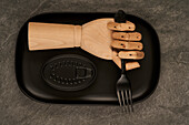 Künstliche Holzhand mit Gabel auf Tablett neben versiegelter schwarzer Dose mit Konserven auf Tisch