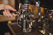 Crop anonymous male barista attaching portafilter with ground espresso coffee on coffee machine in kitchen