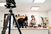 Unrecognizable woman taking photo of chocolate muffins on digital camera against blogger talking during cooking process in kitchen