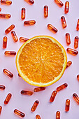 Top view composition of ripe cut oranges arranged on pink surface near scattered pills in light studio