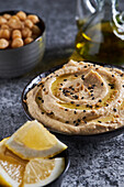 From above slices of fresh lemon placed on gray marble table near bowl of hummus with oil and sesame in kitchen