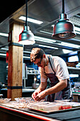 Young serious chef man in cooking apron serving meal in dishes on restaurant kitchen