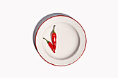 Top view composition of bowl with hot peppers with green stem placed on white background