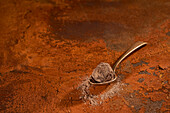 Komposition von oben auf kleinem Metalllöffel mit köstlichem Schokoladentrüffel und Kakaopulver auf rostigem Untergrund