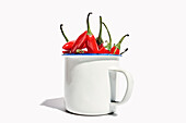 Big ceramic mug full of ripe fresh exotic pepper placed on white background