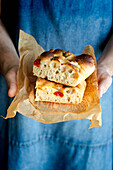 Crop person hands holding piece of fresh tomato focaccia with rosemary