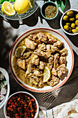 Top view of traditional Greek tasty beef stew with lemon served on table with olives and spices in light kitchen