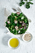 Blick von oben auf einen frischen, gesunden Gemüsesalat in einer Schüssel auf dem Tisch mit Olivenöl und Sonnenblumenkernen